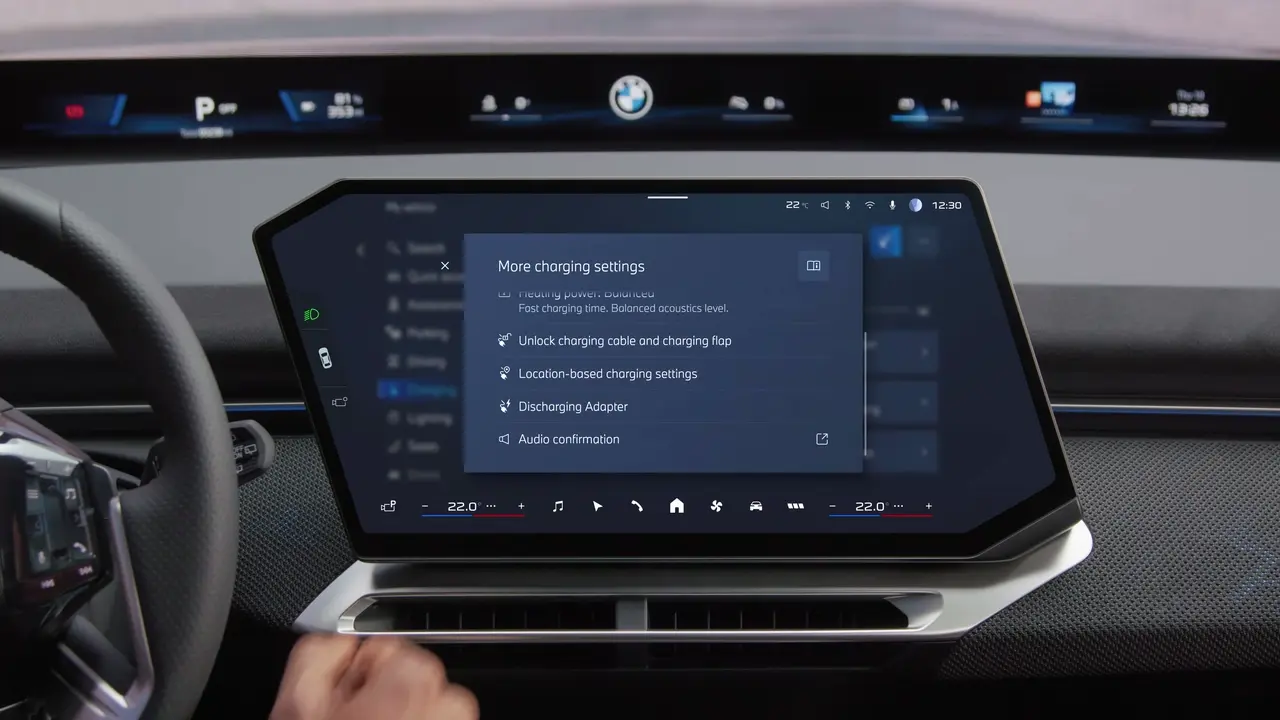 BMW presenter holding the vehicle-to-load cable next to an e-bike and the rear of the iX3