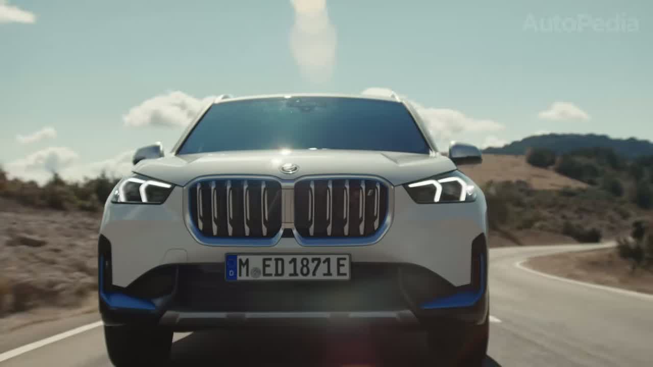 Front view of a white BMW iX1 with the signature kidney grille and blue accents on a German country road.