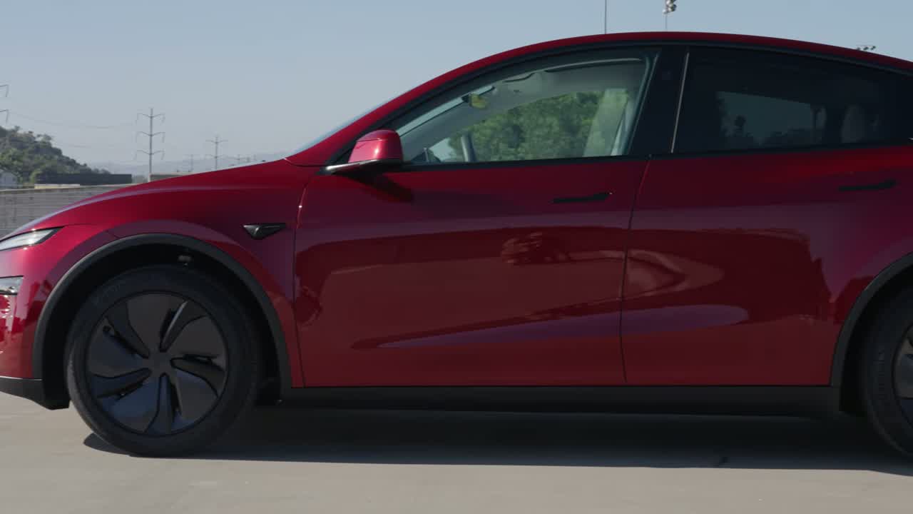 Side profile of the Model Y L showing the longer wheelbase, flush door handles, and aero wheel design on a red paint