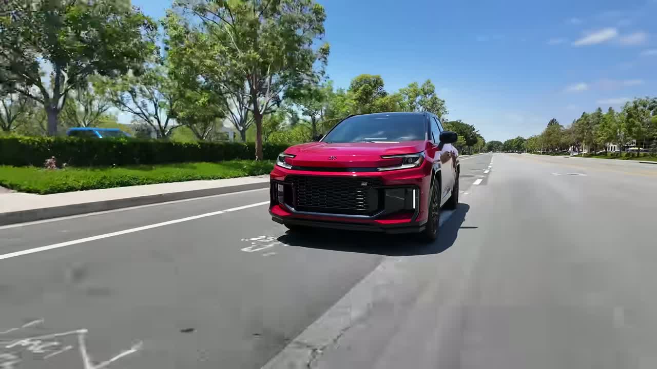 2026 Toyota RAV4 Plug-in Hybrid GR Sport in red, front three-quarter view driving on a suburban street, showing the unique grille, black wheels and lower lip spoiler.