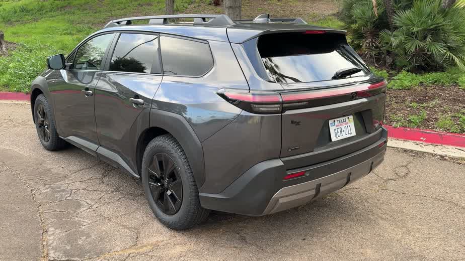 Rear three-quarter view of the gray 2026 Toyota bZ Woodland, showing the separated bZ and Woodland badges and the full-width LED light bar across the tailgate