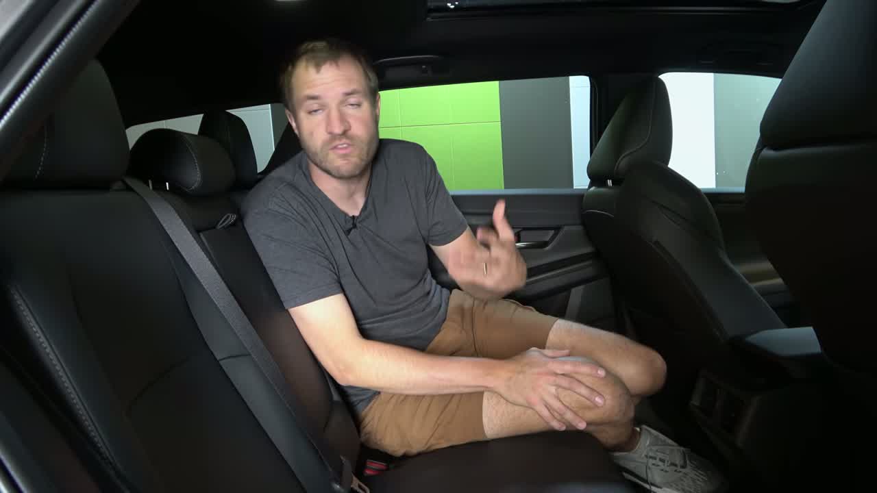 Doug DeMuro sitting in the back seat of the bZ Woodland to demonstrate legroom, with heated rear seats and two USB-C ports visible