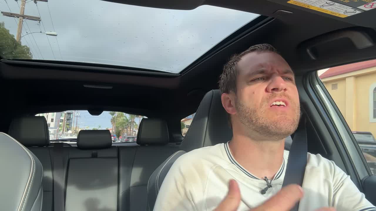 Doug DeMuro driving the bZ Woodland with the panoramic moonroof open above, showing the Premium trim's glass roof